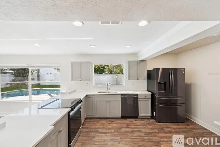 A kitchen with a black refrigerator, white countertops, and wooden flooring.