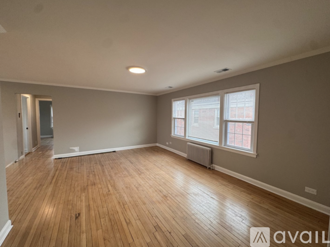 A spacious room with wooden flooring and a window with blinds.