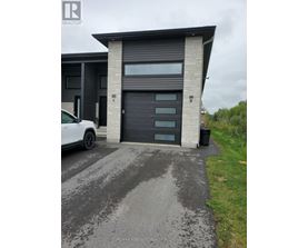 A white car is parked in front of a modern house with a black garage door.