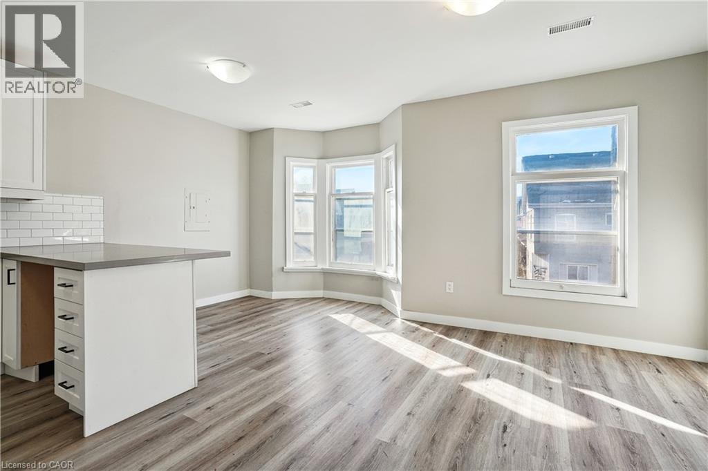 A well-lit, spacious kitchen and living room with wood flooring and white cabinetry.