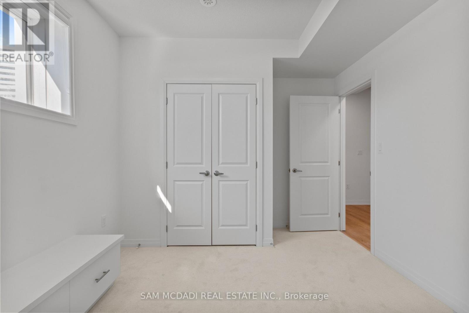 A white bedroom with two doors and a window.