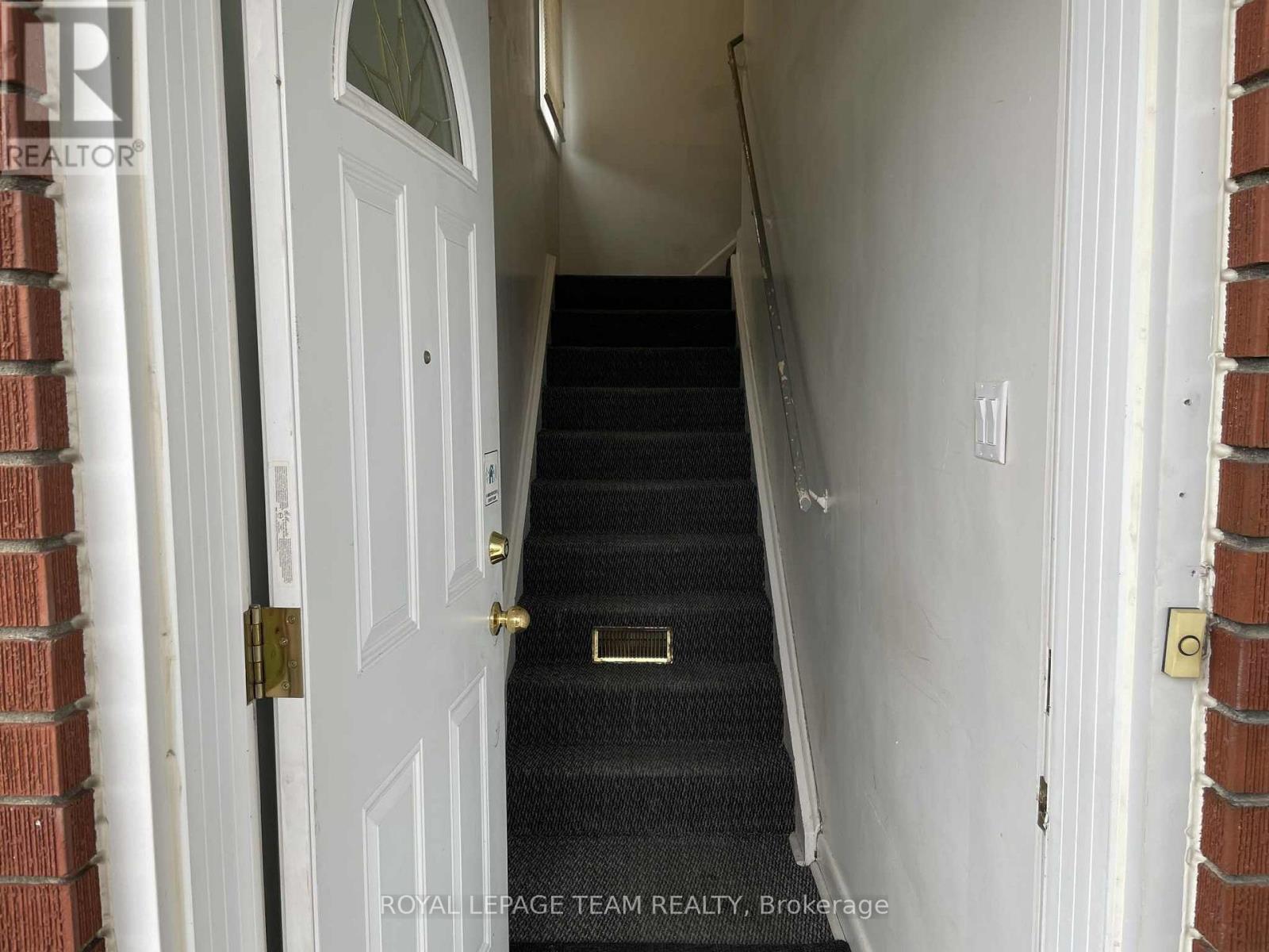 A staircase with a black carpeted runner leads up to a white door.