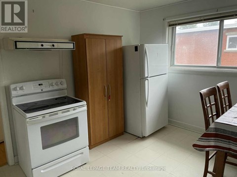 A kitchen with a white oven, a white fridge, a wooden cabinet and a window.
