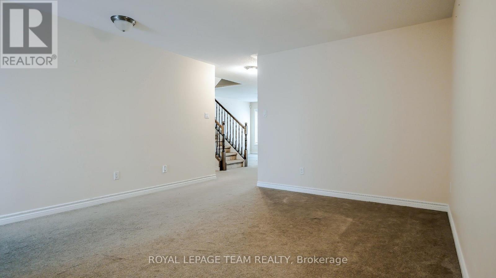 A spacious room with a carpeted floor and a staircase in the background.