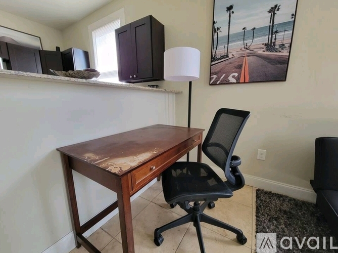 A wooden desk with a black chair in front of a wall with a painting of a beach scene.