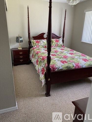 A four poster bed with a floral bedspread sits in a bedroom with a nightstand and lamp.