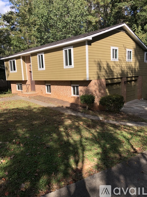 A house with a brown and beige exterior is surrounded by greenery.