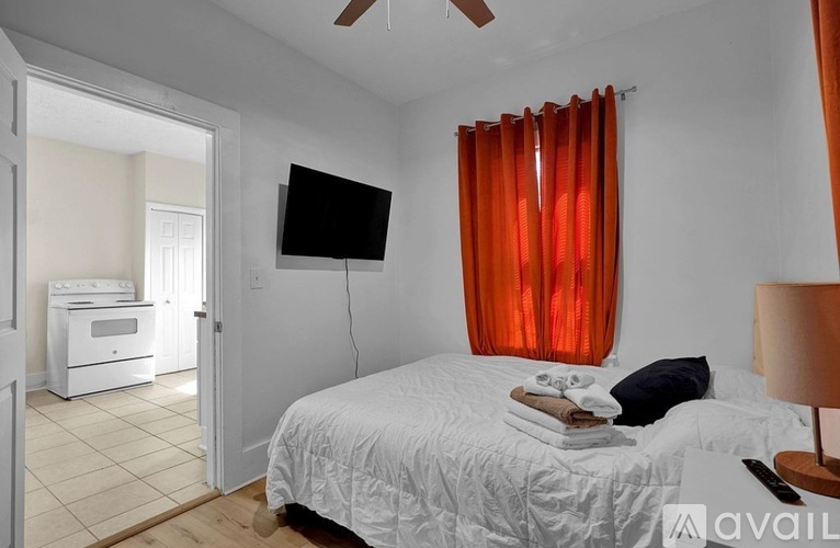 A bedroom with a bed, a television, and a window with red curtains.
