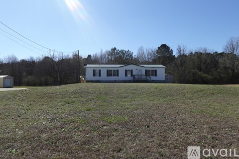 A house is situated in a field with trees in the background.