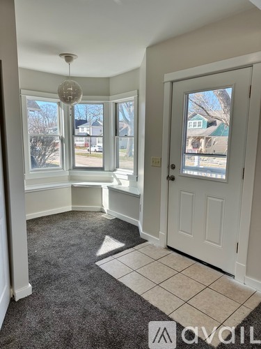 A room with a carpeted floor, a white door, and a window seat.
