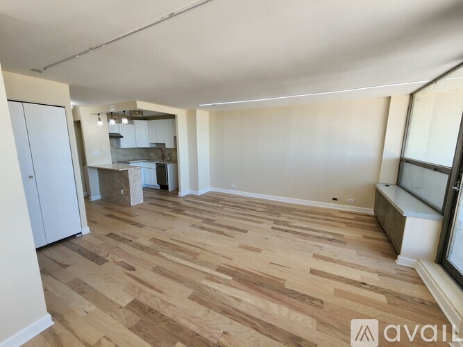 A room with wooden flooring and a kitchen area in the background.