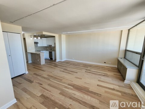 A room with wooden flooring and a kitchen area in the background.