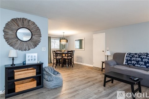 A living room with a grey couch, a wooden coffee table, a round mirror, and a dining table with chairs.