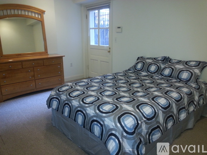 A bed with a blue and white patterned comforter sits in a bedroom with a wooden dresser and mirror.