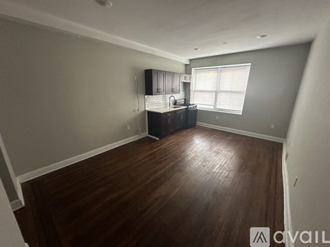A spacious room with wooden flooring and a kitchenette in the corner.