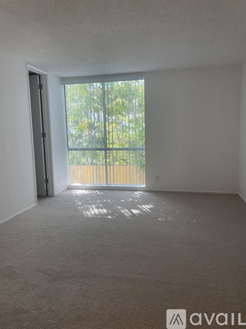 A room with a carpeted floor and a door leading to a balcony with a view of trees.