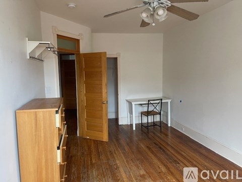 A room with a wooden floor, a white table with a chair, and a ceiling fan.