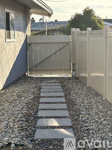 A white gate is open to a gravel path.
