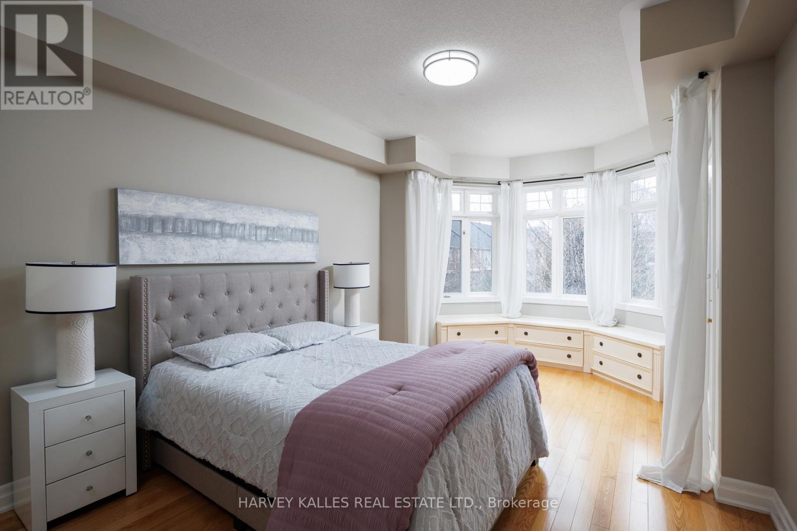 A bedroom with a large bed and a window with white curtains.