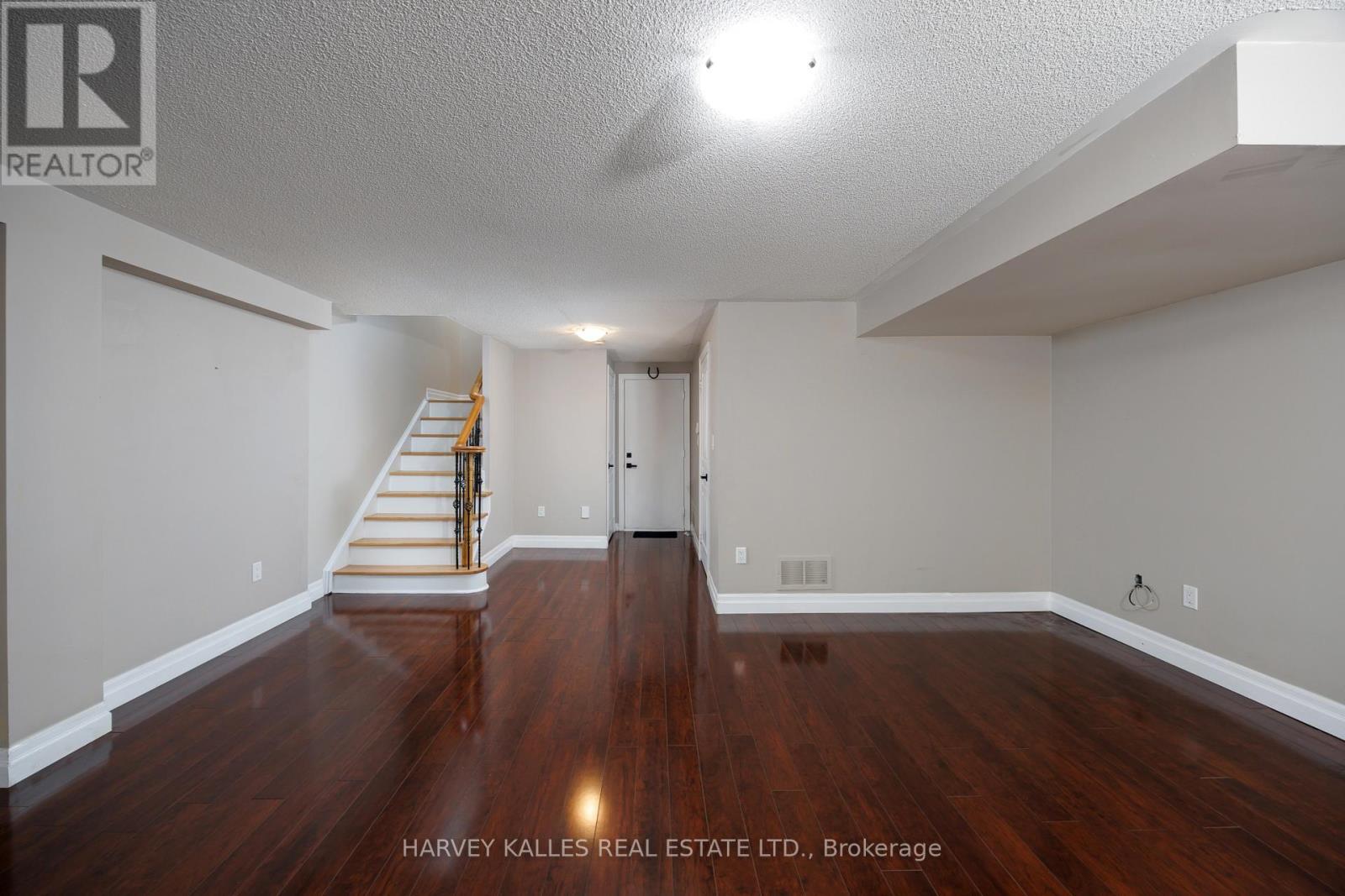 A spacious room with wood flooring and a staircase leading to another level.