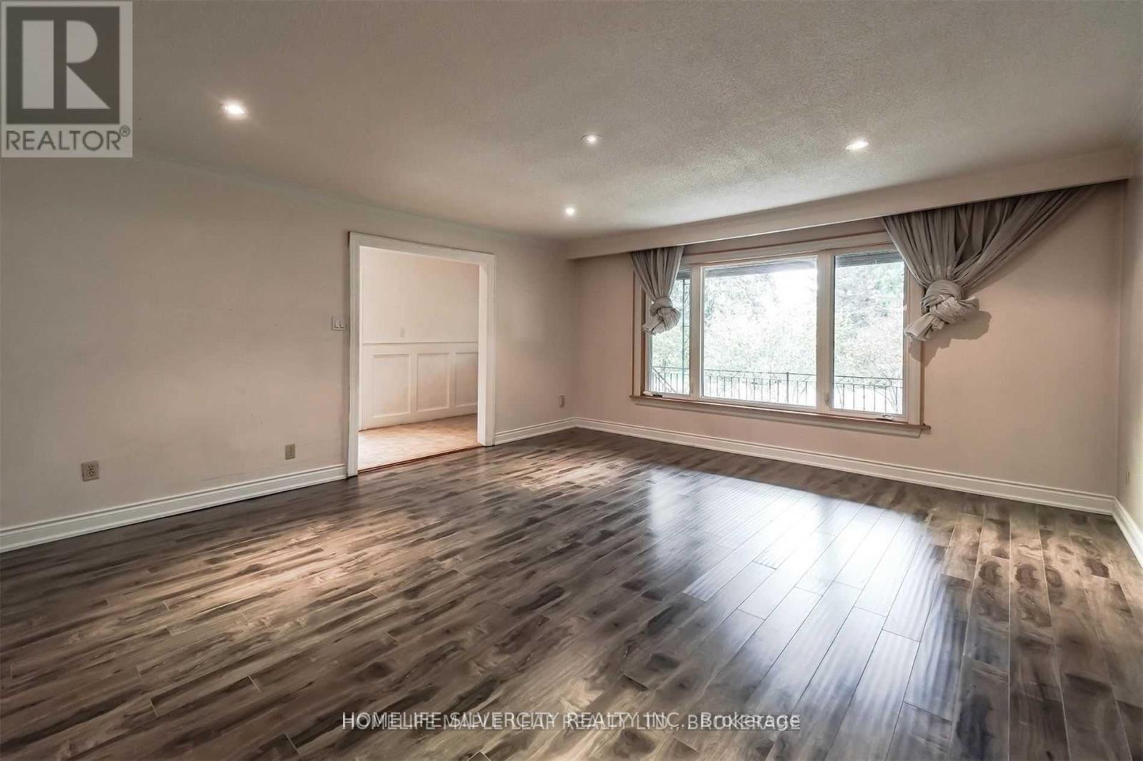 A spacious room with wooden flooring and a large window.