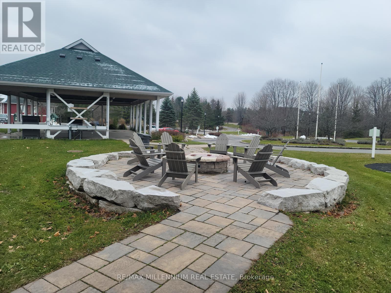A gazebo is surrounded by a stone wall and chairs are placed around a fire pit.