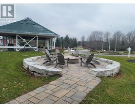 A gazebo is surrounded by a stone wall and chairs are placed around a fire pit.