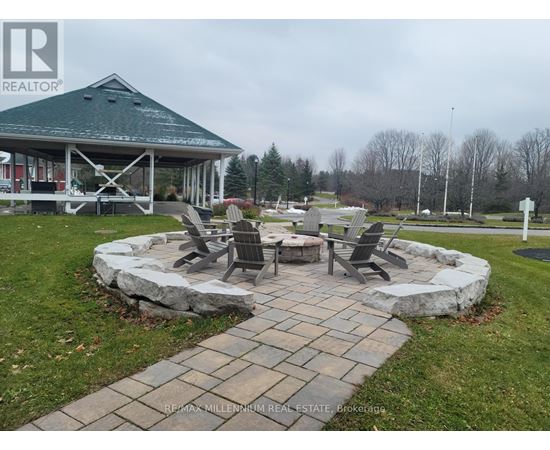 A gazebo is surrounded by a stone wall and chairs are placed around a fire pit.