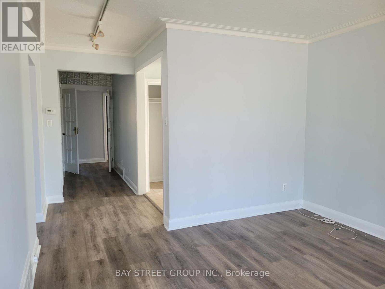 A room with a wooden floor and white walls, with a doorway leading to another room.