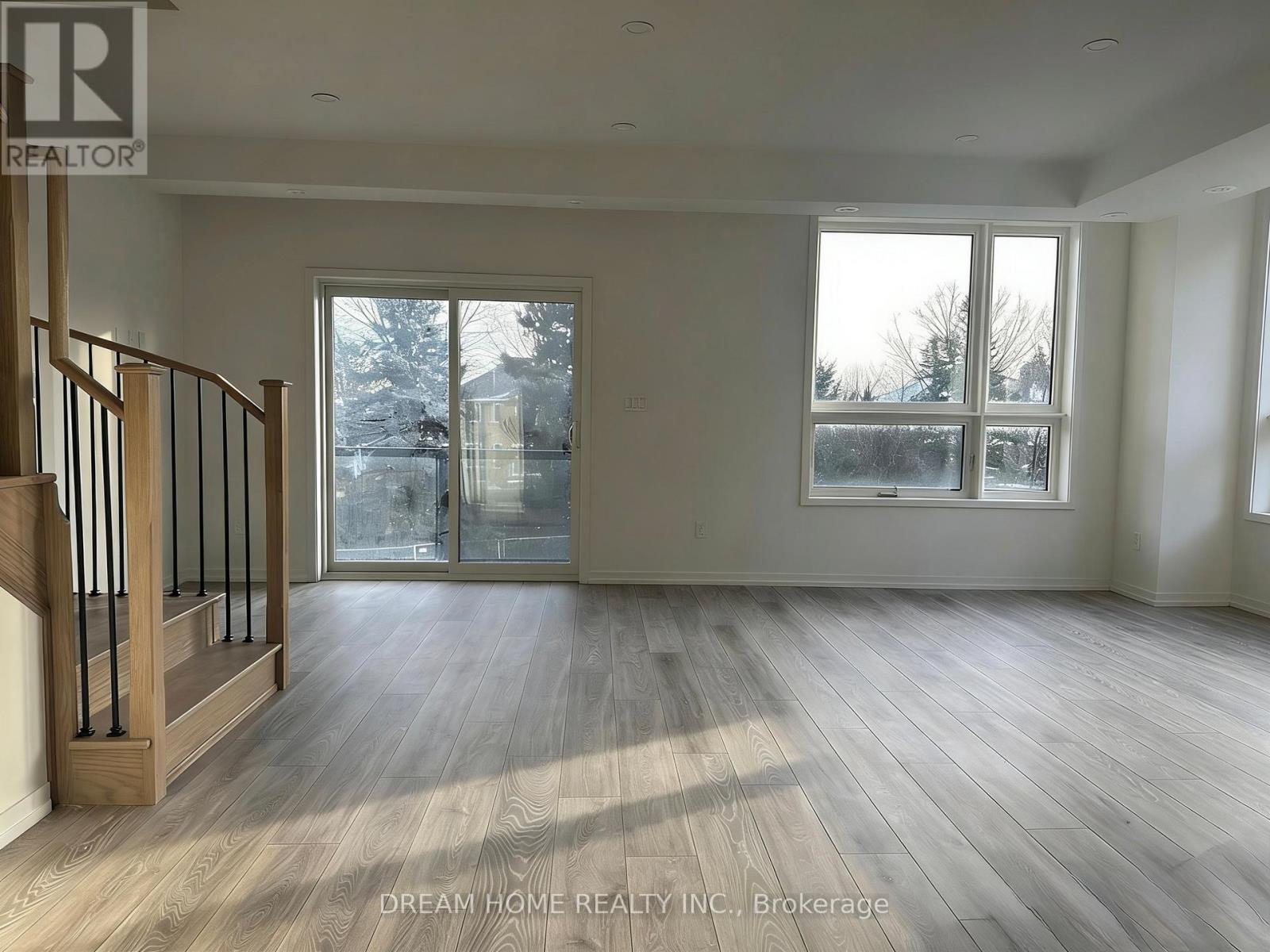 A spacious room with wooden flooring and a staircase on the left side.