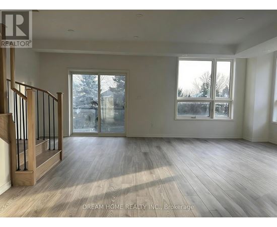 A spacious room with wooden flooring and a staircase on the left side.