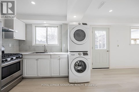 A white washing machine is in a kitchen with white cabinets.