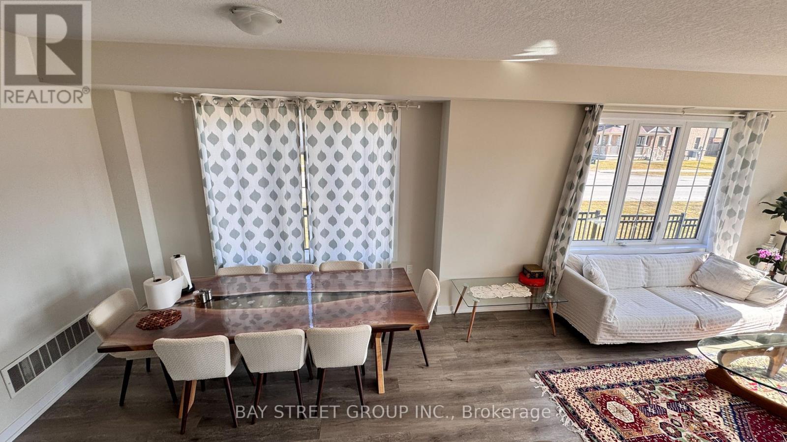 A dining room with a glass table and chairs, a sofa, and a rug.