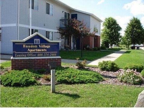 A sign for Freedom Village Apartments in front of a building.