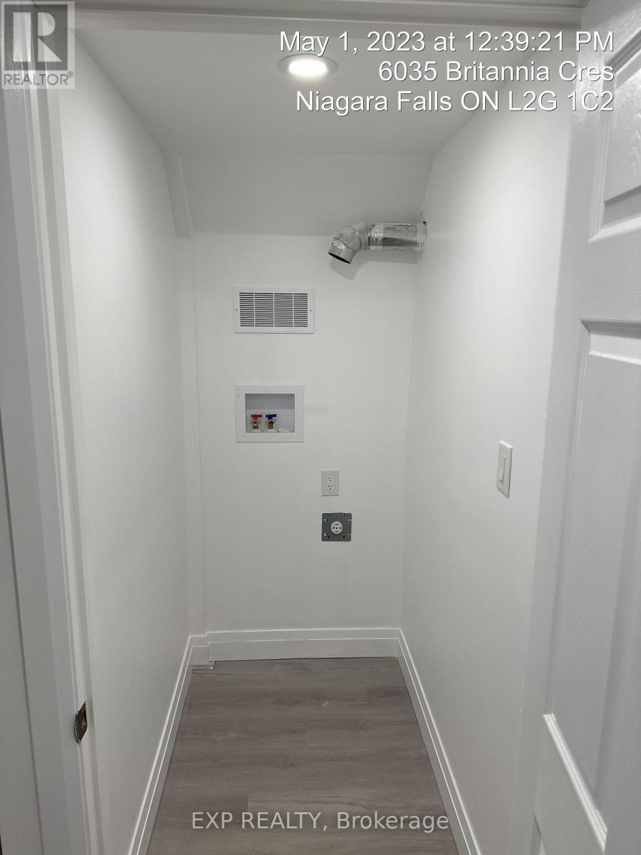 A white hallway with a door on the left and a wall-mounted light switch.