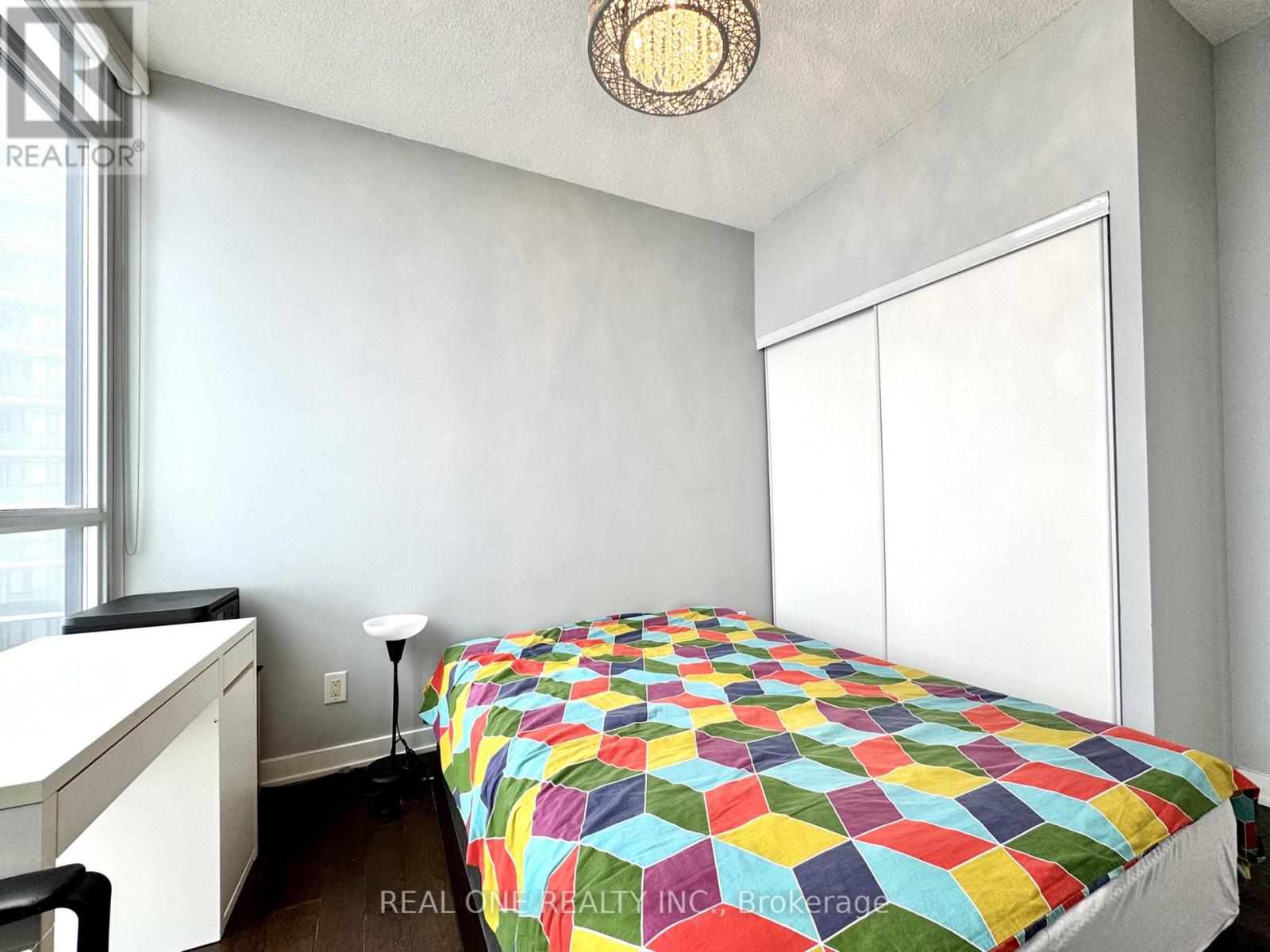 A bedroom with a bed covered in a multicolored quilt.