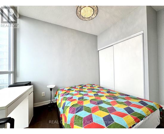 A bedroom with a bed covered in a multicolored quilt.