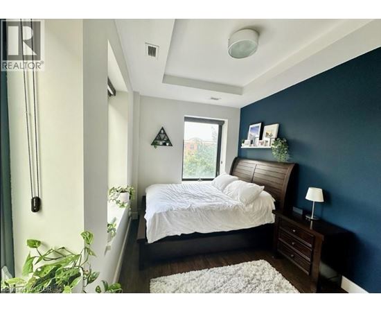 A bedroom with a bed, nightstand, and a plant.