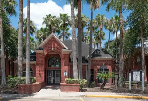 A red brick building with a black door and windows surrounded by palm trees.