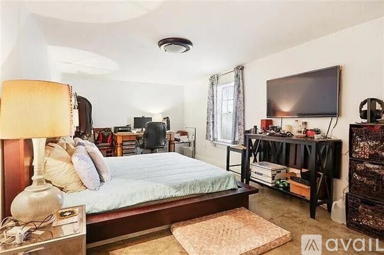 A bedroom with a bed, a nightstand with a lamp, a TV, and a shelf with various items.