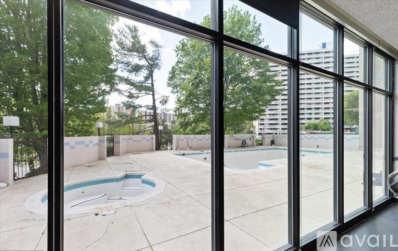 A view of a pool through a window with trees and buildings in the background.