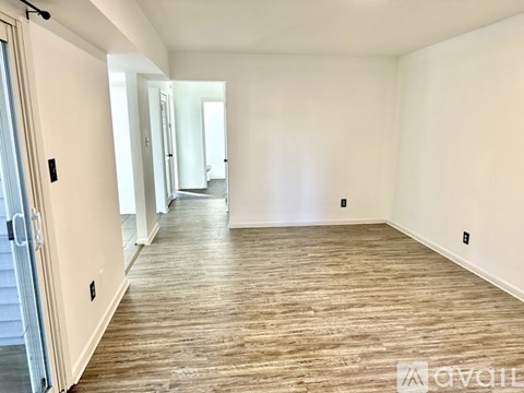 A spacious room with wooden flooring and white walls.