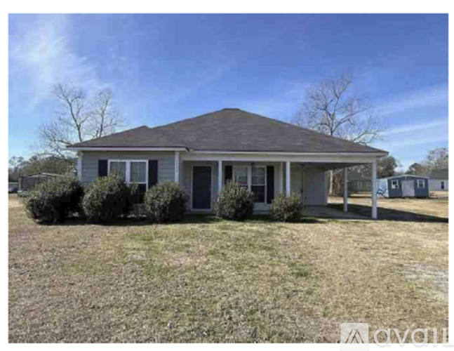 A small house with a gray roof and a front yard with bushes.