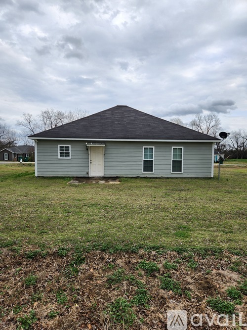 A house with a grey roof and a white door is surrounded by a grassy field.