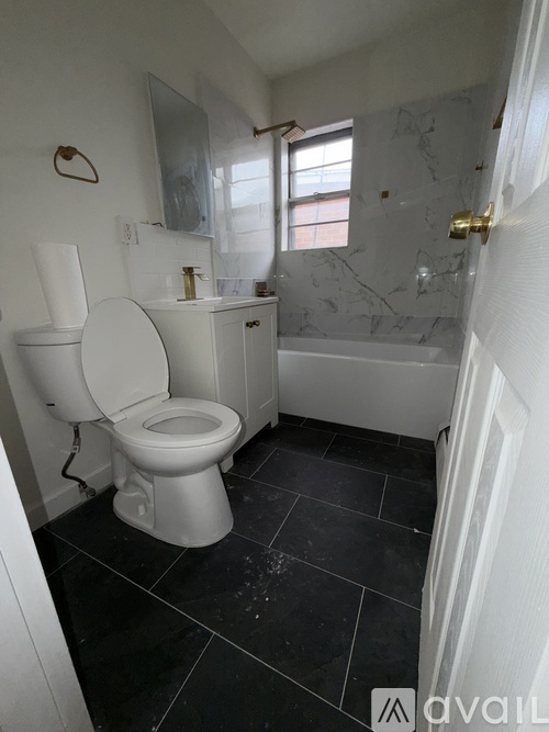 A white toilet sits in a bathroom with black tile flooring.
