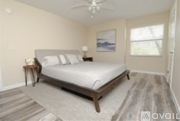 A bedroom with a bed, a fan, and a painting on the wall.