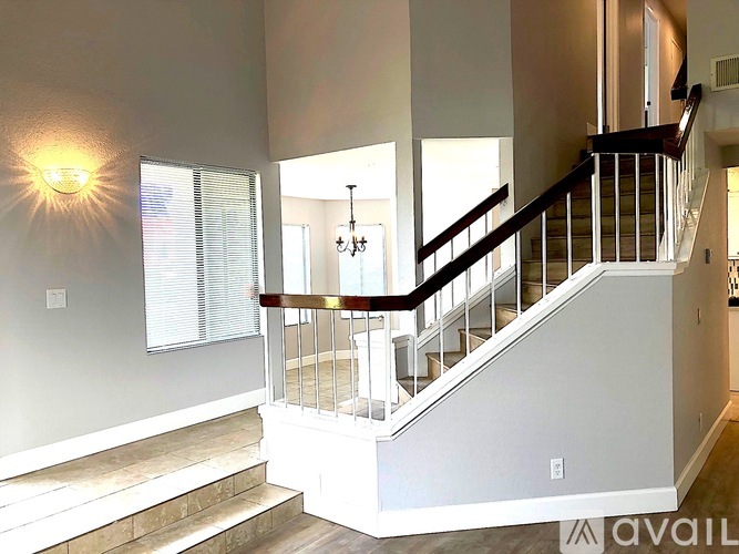 A well-lit staircase with a chandelier and a window with blinds.