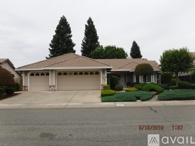 A house with a brown roof and a garage door is surrounded by trees and bushes.