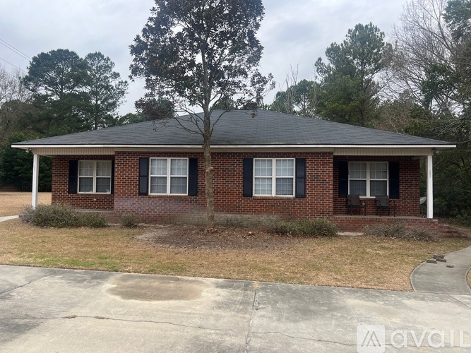 A small brick house with a black roof and a tree in front.
