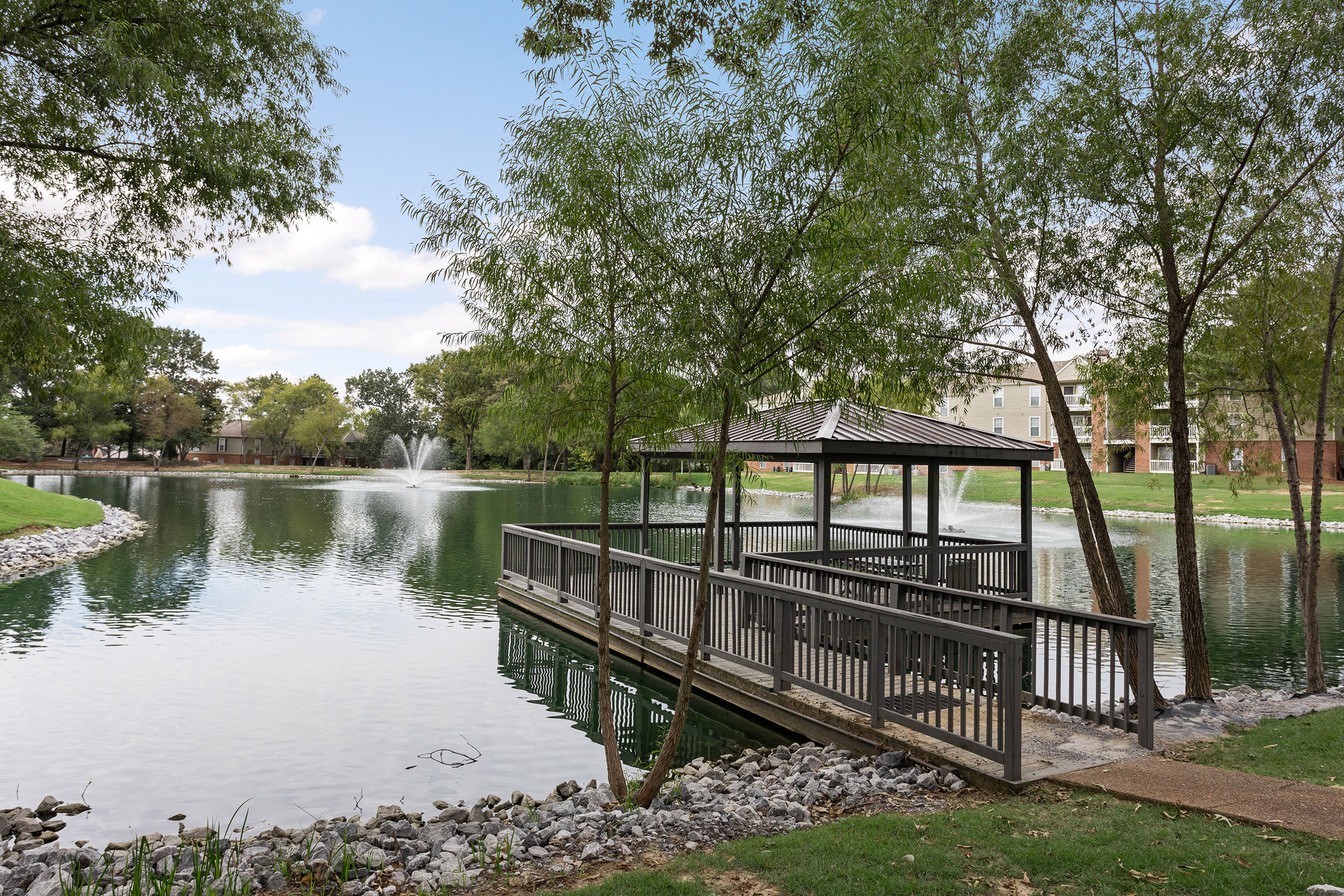 Covered dock with stunning view of large pond and shade trees on apartment grounds